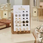 Elegant stud earrings set with gold, black, and crystal designs displayed on a wooden stand