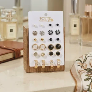 Elegant stud earrings set with gold, black, and crystal designs displayed on a wooden stand