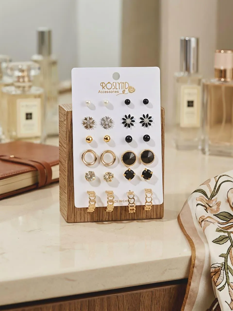 Elegant stud earrings set with gold, black, and crystal designs displayed on a wooden stand