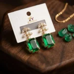 Elegant green stone earrings with gold setting and crystal leaf design displayed on wooden surface