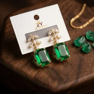 Elegant green stone earrings with gold setting and crystal leaf design displayed on wooden surface