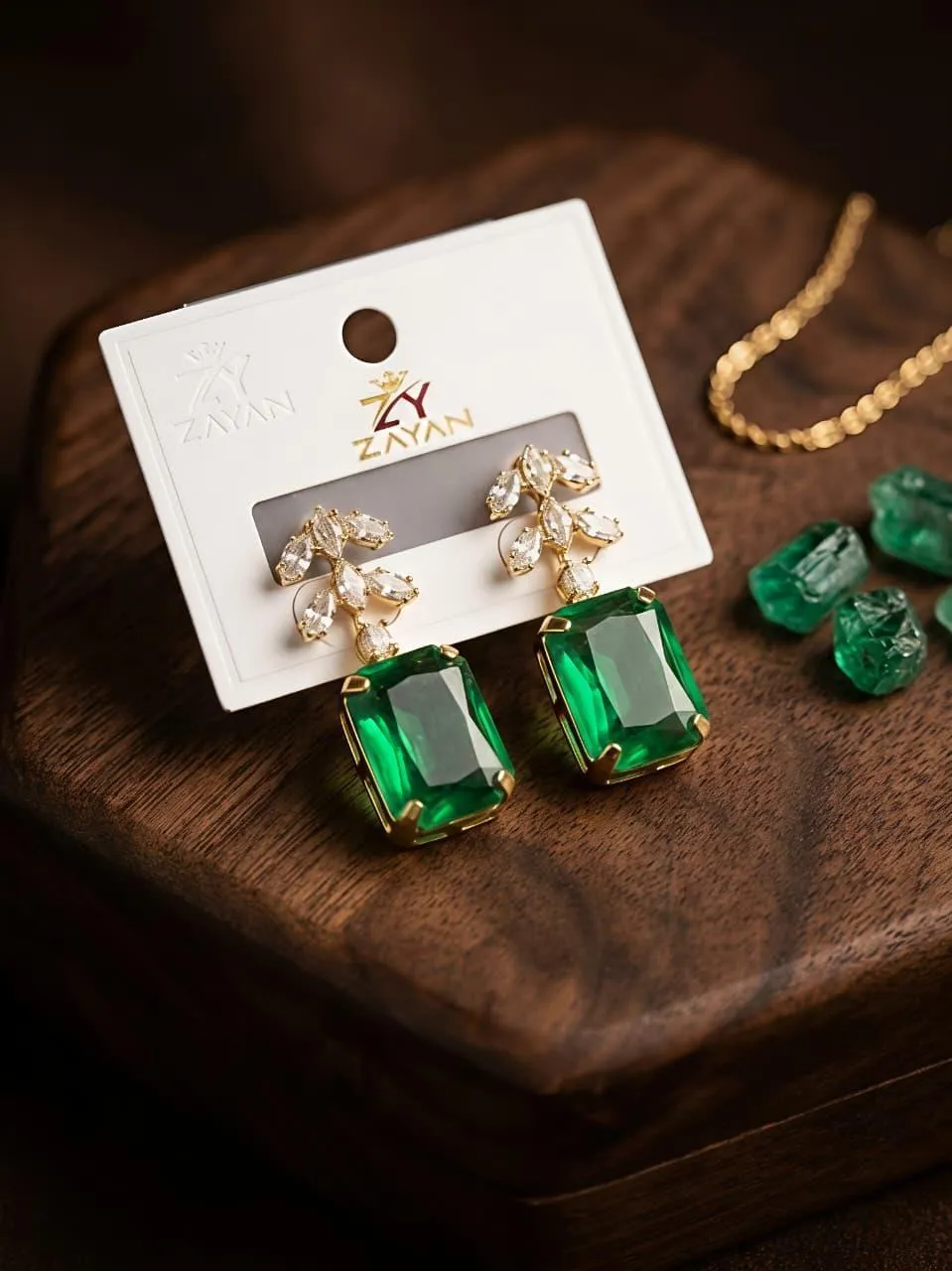 Elegant green stone earrings with gold setting and crystal leaf design displayed on wooden surface